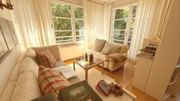 Helles Wohnzimmer mit bequemer Sitzecke, Parkettboden und großen Fenstern mit Blick ins Grüne.