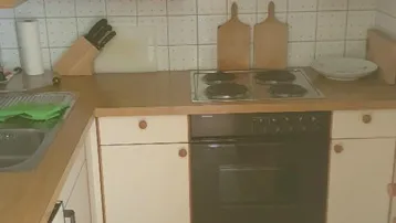 Funktionale Küche mit hellen Holzschränken, Elektroherd und weiß gefliestem Spritzschutz.