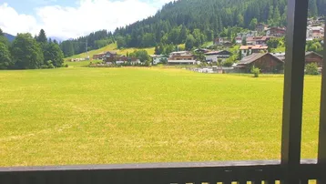 Weitläufiger Blick von einem Balkon auf grüne Wiesen und eine Berglandschaft mit Häusern.