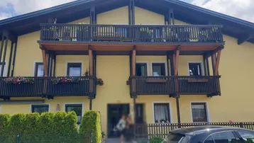 Traditionelles Gebäude mit gelber Fassade und mehreren Holzbalkonen, geschmückt mit Blumenkästen.