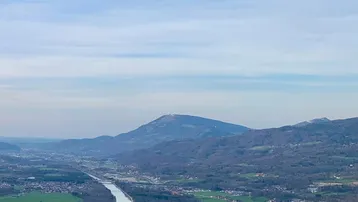 Weitläufige Luftaufnahme eines Flusses, der sich durch eine grüne Landschaft mit Bergen und Siedlungen schlängelt.
