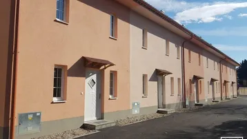 Reihenhäuser mit hellen Fassaden und Vordächern unter blauem Himmel, in einer ruhigen Wohngegend.