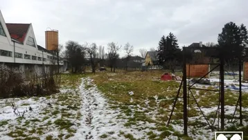 Weitläufiges Grundstück mit Gras und Schnee, umgeben von Bäumen und anderen Gebäuden in der Ferne.