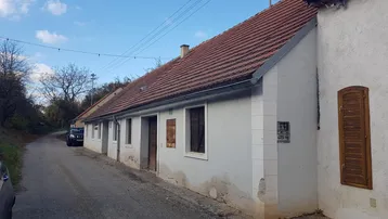 Ländliches Gebäude mit Ziegeldach und einfacher Fassade entlang einer unbefestigten Straße.