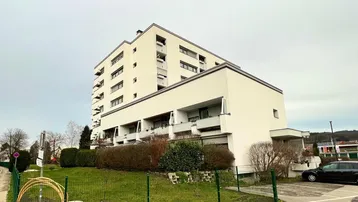 Modernes Mehrfamilienhaus mit mehreren Balkonen und gepflegter Grünanlage in städtischer Umgebung.