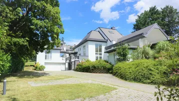 Moderne Villa mit weißer Fassade, großem Garten und gepflasterter Auffahrt unter blauem Himmel.