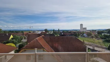 Weitblick über Dächer und ländliche Umgebung von einem Balkon aus unter blauem Himmel.