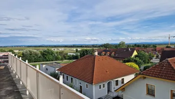 Weitläufiger Blick über eine ländliche Wohngegend mit Feldern und Häusern unter blauem Himmel.