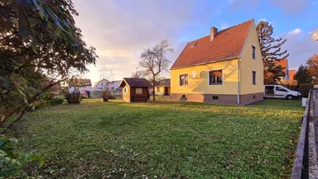 Großzügiger Gartenbereich mit Rasenfläche und einem kleinen Gartenhaus bei Sonnenuntergang.