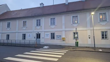 Historisches Gebäude mit mehreren Fenstern und einem Zebrastreifen davor, bei Dämmerung aufgenommen.