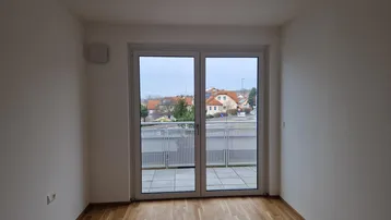 Lichtdurchfluteter Raum mit Holzboden und Zugang zu einer Terrasse mit Blick ins Grüne.