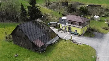 Luftaufnahme eines gelben Hauses und einer Scheune in einer grünen, ländlichen Umgebung.