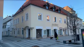 Historisches Gebäude mit heller Fassade und rotem Ziegeldach an einer gepflasterten Straße.