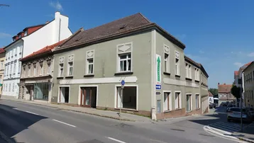 Historisches Gebäude an einer Straßenecke mit mehreren Fenstern und einem Geschäft im Erdgeschoss.