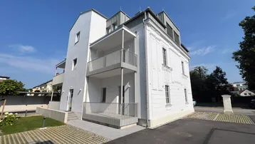 Ansicht des modernen Gebäudes mit Balkonen und historischer Fassade unter blauem Himmel.