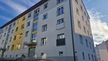 Mehrstöckiges Wohngebäude mit moderner Fassade in Grau und Gelb unter blauem Himmel.