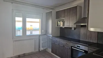 Funktionale Küche mit dunklen Holzfronten, Fliesenboden und Fenster mit Rollladen.