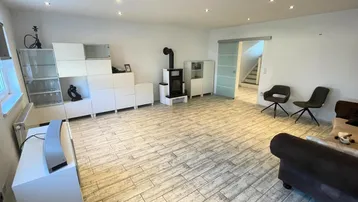 Heller Wohnbereich mit modernem Kaminofen, Fliesenboden und Schiebetür zum Treppenhaus.