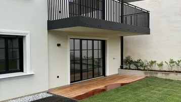 Moderne Hausfassade mit Balkon, Holzterrasse und frisch angelegtem Rasenbereich.