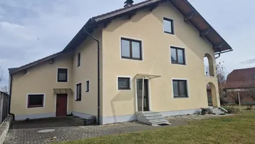 Vorderansicht des Hauses mit beiger Fassade, braunen Fenstern und gepflegtem Vorgarten.