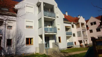 Mehrfamilienhaus mit hellblauer Fassade, Balkonen und einem kleinen Vorgartenbereich.