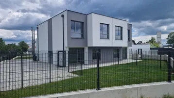 Seitenansicht eines modernen Reihenhauses mit gepflegtem Rasen und Zaun.