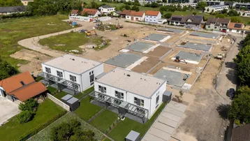 Luftaufnahme eines Neubaugebietes mit bereits fertiggestellten Reihenhäusern und weiteren im Bau befindlichen Fundamenten.