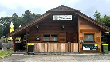 Rustikales Holzgebäude mit traditioneller Architektur und einem kleinen Außenbereich unter bewölktem Himmel.