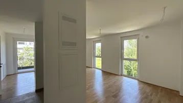 Helles, leeres Zimmer mit Holzboden und Zugang zu einem Balkon, ideal für Wohnzwecke.