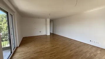 Helles, leeres Zimmer mit Holzboden und Zugang zu einem Balkon oder einer Terrasse.