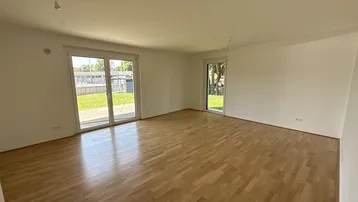 Helles, leeres Wohnzimmer mit Holzboden und großen Schiebetüren zum Garten.