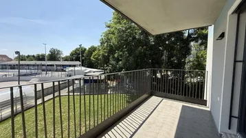 Geräumiger Balkon mit Blick auf Sportanlagen und viel Grün unter blauem Himmel.