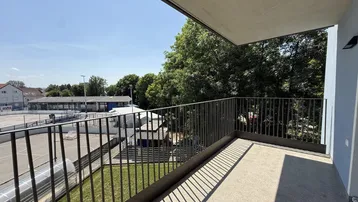 Geräumiger Balkon mit Blick auf einen Sportplatz und umliegende Bäume unter blauem Himmel.