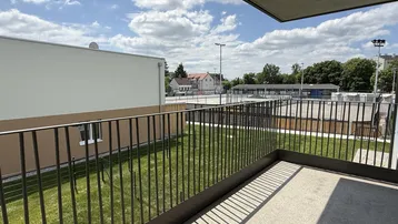 Geräumiger Balkon mit Blick auf Sportanlagen und grüne Umgebung unter blauem Himmel.