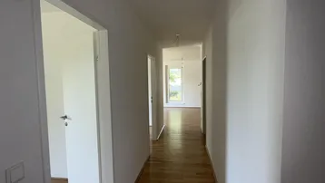 Langer, heller Flur mit Holzparkettboden und Blick in weitere Zimmer mit Tageslicht.