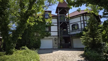 Traditionelles Fachwerkhaus mit zwei Garagen und begrüntem Eingangsbereich unter blauem Himmel.