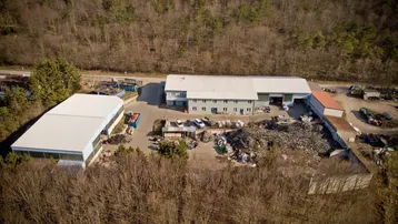 Luftaufnahme eines Gewerbeobjekts mit mehreren Hallen und Freiflächen, umgeben von Wald und Natur.