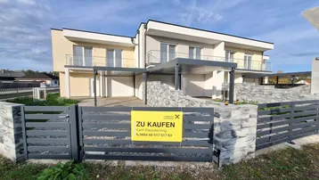 Moderne Reihenhäuser mit Carports und Steinmauern, umgeben von einem Zaun, stehen zum Verkauf.