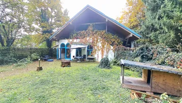 Charmantes Haus mit großem Garten, umgeben von Bäumen und einer kleinen Terrasse.