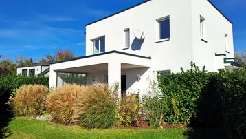 Modernes weißes Haus mit Flachdach, umgeben von einem gepflegten Garten mit Ziergräsern.