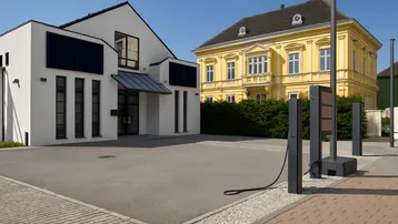 Außenansicht des modernen Gebäudes mit Ladestation für Elektrofahrzeuge und gepflastertem Vorplatz.