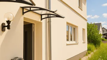 Hauseingang eines modernen Neubaus mit Vordach und gepflegter Außenanlage.