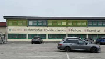 Moderne Außenansicht eines Geschäftsgebäudes mit grünen Fensterrahmen und einem weitläufigen Parkplatz davor.