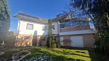 Einfamilienhaus mit gepflegtem Vorgarten und Photovoltaikanlage auf dem Dach an einem sonnigen Wintertag.