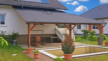 Gartenbereich mit überdachter Terrasse, kleinem Pool und viel Grün unter blauem Himmel.