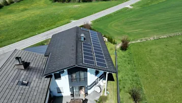 Dachansicht des Hauses mit Photovoltaikanlage und einer möblierten Terrasse im Garten.
