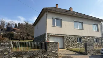 Ansicht des Hauses von der Straße mit Steinfassade und Garageneinfahrt unter blauem Himmel.