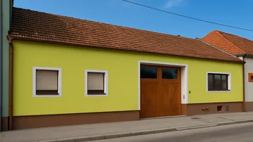 Gelb gestrichenes Haus mit braunem Dach und Holztor, direkt an der Straße gelegen.