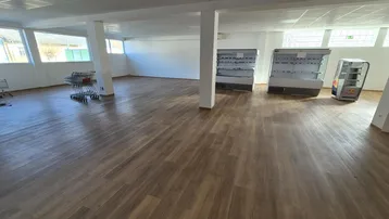 Geräumiger Ladenbereich mit neuem Laminatboden, großen Fenstern und Kühlregalen, ideal für Einzelhandel.