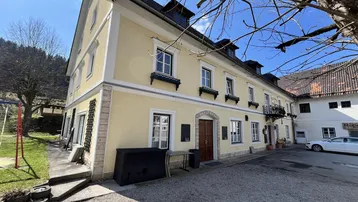 Gelbe Fassade eines traditionellen Gebäudes mit mehreren Fenstern und einem Eingangsbereich.